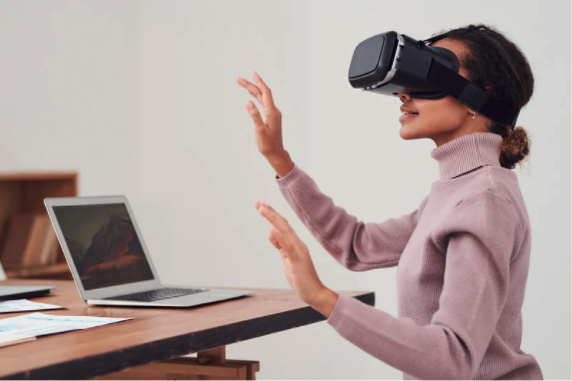 woman using a VR headset as she stands near a table with a laptop and some papers