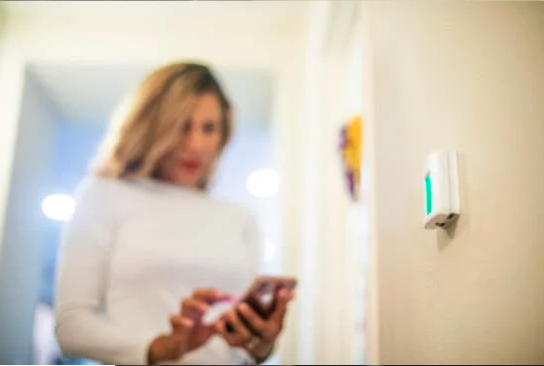 woman using mobile phone near thermostat