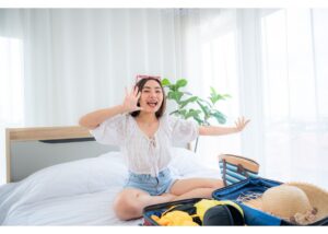 Gen Z guest in hotel room, sitting on bed with open luggage