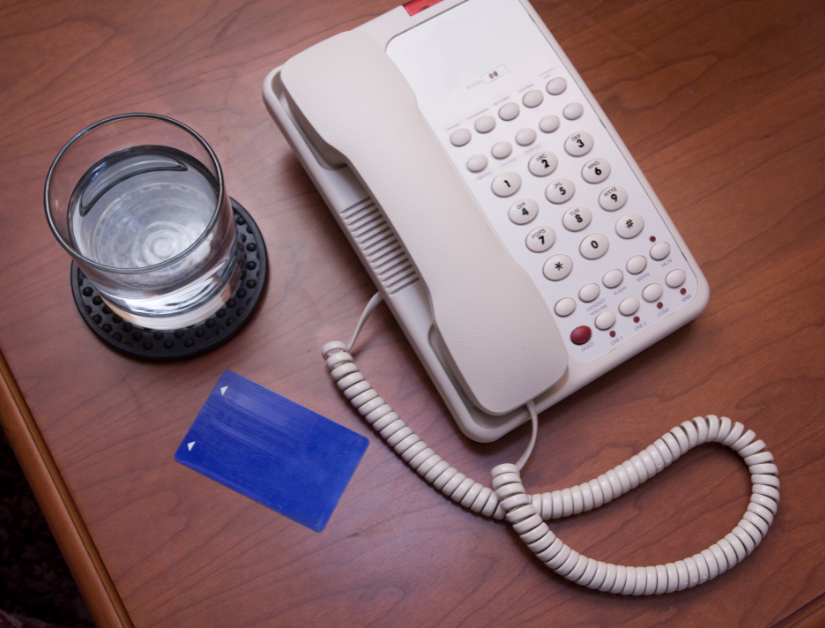VoIP phone on bedside stand with glass of water and room key card