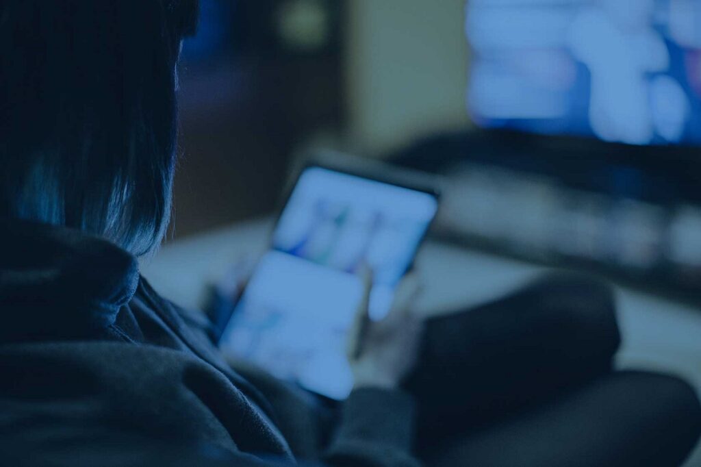 person viewing tablet and TV in darkened room